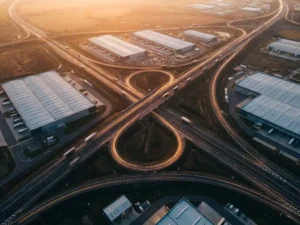 Aerial view of highway network with delivery trucks on glowing amber route pathways connecting modern distribution warehouses at dusk
